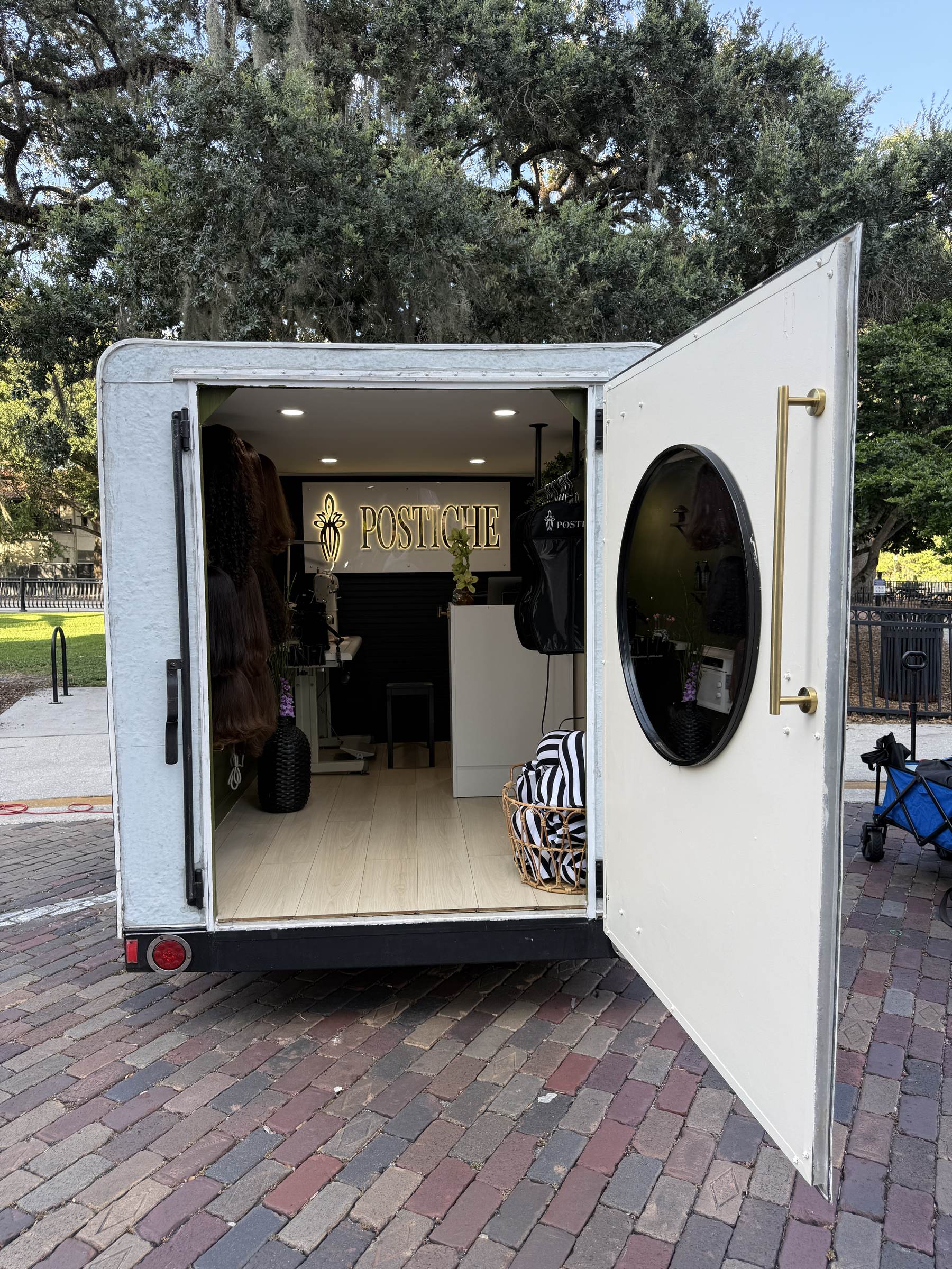 Inside the Postiche Traveling Studio, with the illuminated Postiche sign, styling station, and mirror on the open door